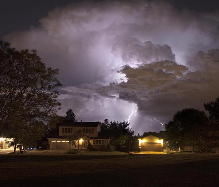 At night as rain falls and stars shine in the distance, lightning bolts strike over  suburban homes and trees